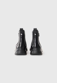 Bottines en cuir noir avec une finition lisse, présentant un bout arrondi et des panneaux latéraux élastiques, accentuées par un logo argenté et des languettes de tirage.
