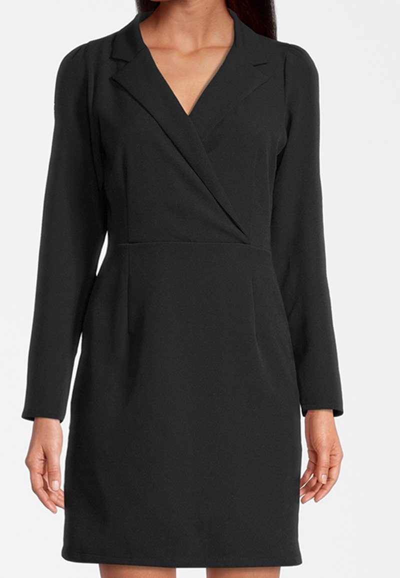 Robe noire à manches longues style portefeuille avec col à revers portée par une femme, cintrée à la taille, longueur genou.