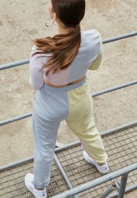 Souprava teplákové soupravy s barevnými bloky ve světlé šedé, pastelové žluté a růžové barvě. Pohodlný materiál s elastickým pasem, nošená s bílými teniskami.