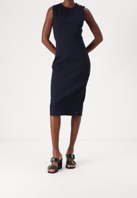 Granatowa dopasowana sukienka midi bez rękawów. Posiada guziki na ramionach oraz kontrastowe szwy. Zestawiona z czarnymi sandałami na obcasie.