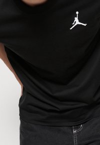 T-shirt in cotone nero con logo Jumpman bianco sul petto, colletto girocollo e vestibilità rilassata. Texture liscia e design semplice.