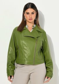Veste cropped en simili cuir vert avec un col en V, des poches zippées et des manches longues. Texture lisse et silhouette moderne.