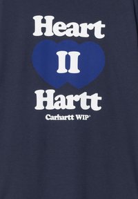 Camiseta de algodón azul marino con un atrevido texto blanco que dice "Heart II Hartt" junto con un gráfico de corazón azul y el logo de "Carhartt WIP" en la parte inferior.