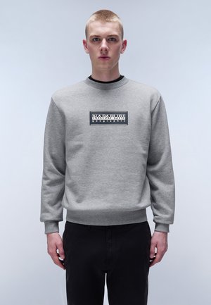 Sudadera gris con cuello redondo, puños y cintura acanalados. Cuenta con un logotipo rectangular negro en la parte frontal con texto blanco.