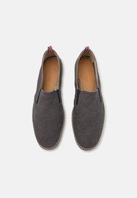 Des chaussures slip-on grises en tissu, avec des panneaux latéraux élastiques, une semelle intérieure beige texturée et une semelle contrastante cousue. Étiquette d'accent rouge et bleue.