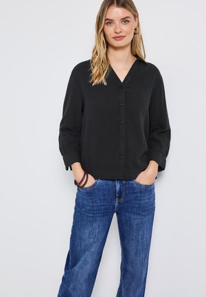 Chemise noire à col avec un bouton sur le devant et des manches trois-quarts, associée à un jean en denim bleu à pattes d'éléphant. Texture lisse dans l'ensemble.