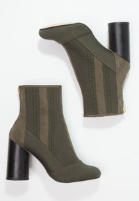 Booty w kolorze oliwkowym z teksturowanym cholewką z dzianiny, solidnymi akcentami z zamszu i masywnym czarnym obcasem. Zawiera zamek błyskawiczny z boku.