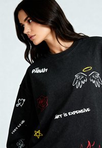 Felpa nera oversize con vari motivi ricamati, tra cui cuori, rose e testo in bianco, rosso e giallo. Collo a costine.