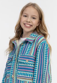 Monivärinen kuvioitu takki, joka on valmistettu teksturoituneesta kankaasta. Takissa on sinisiä, vaaleanpunaisia ja vihreitä sävyjä, kultaiset napit ja etupocketsit.