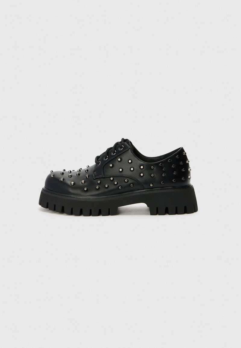 Pantofi platform din piele neagră cu detalii cu ținte, având vârful rotund, șireturi și o talpă groasă, zimțată pentru aderență.