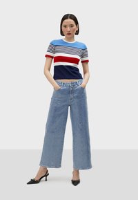 Randig stickad topp med blå, röda och vita nyanser, kombinerad med ljusblå vida jeans och svarta kitten heels med dekorativa detaljer.