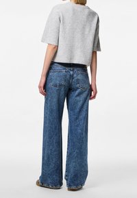 Šedý žebrovaný zkrácený svetr s širokými krátkými rukávy, kombinovaný s volnými modrými džíny s vysokým pasem. Oblečení má uvolněnou strukturu.