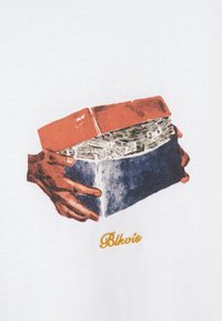 Deux mains brunes tenant un bloc composé de briques superposées, de matériau ondulé et de pierre bleue avec le texte « Blkvic » en dessous.