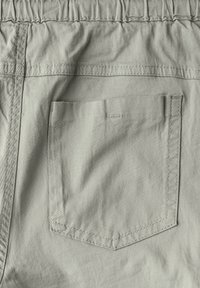 Ljusgrått tyg på bakfickan, rektangulär form med synlig söm. Har ett elastiskt midjeband och en slät yta.