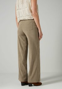 Lichtbruine corduroy wijde broek met verticale ribbels, gecombineerd met een crèmekleurige textuurtop en bruine hoge laarzen. Zichtbare achterzakken.