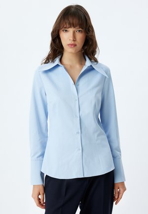 Camisa abotonada azul claro con cuello extendido, con mangas largas y cintura ajustada, hecha de una tela suave, diseñada para un aspecto pulido.