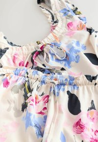 Stof met bloemenpatroon in roze, blauw en zwart. Voorzien van elastische plooien en strikjes bij de halslijn en tailleband voor verstelbaarheid.