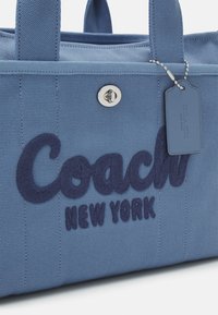 Sac à main en tissu bleu Coach New York avec logo brodé, fermeture tourniquet argentée et étiquette en cuir assortie sur une chaîne à billes en métal.