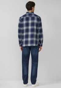 Navyblauw-wit geruit overhemd met lange mouwen, een kraag en knoopmanchetten, gecombineerd met een blauwe spijkerbroek en witte sneakers. Zichtbare stiksel details.