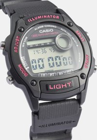 Cyfrowy zegarek Casio z czarną plastikową kopertą i paskiem. Posiada czerwone akcenty, cyfrowy wyświetlacz oraz przyciski oznaczone "LIGHT", "START" i "SPLIT".