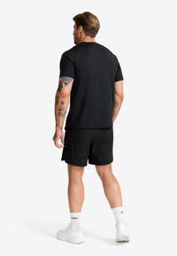 Svart atletisk t-shirt med korta ärmar, kombinerad med svarta shorts. Tyget ser slätt ut och är designat för komfort under sportaktiviteter.
