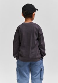 Ciemnoszara bluza z okrągłym dekoltem i luźnym krojem, zestawiona z jasnoniebieskimi spodniami cargo z bocznymi kieszeniami. Czarna czapka noszona do tyłu.