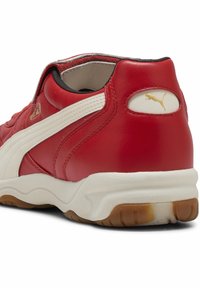 Crvene kožne tenisice s bijelim detaljima i zlatnim logotipom. Zaobljenog oblika, s umućenim ovratnikom i teksturiranom potplatom. Guma na donjem dijelu za bolju prianjanje.