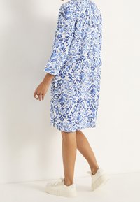 Vestido azul y blanco con estampado, mangas tres cuartos, largo hasta la rodilla, confeccionado con tela ligera, combinado con zapatillas blancas.