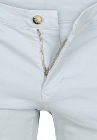 Lichtblauwe denim broek met een metalen ritssluiting en een messing knoop, subtiele stikdetails en een gladde, licht gestructureerde afwerking.