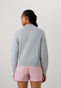 Light gray cable-knit sweater with ribbed hem and collar, worn over pink and white striped shorts. The texture is prominent and detailed.