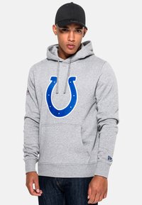 Grauer Kapuzenpulli mit einem großen blauen Indianapolis Colts-Logo auf der Vorderseite, ausgestattet mit einer Kapuze mit Kordelzug und einer Kängurutasche. Schwarze Mütze getragen.