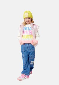 Gilet imbottito rosa, maglione con testo bianco e colorato, pantaloni cargo blu con tasche e sneakers rosa. Berretto di lana giallo brillante.