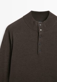 Maglione a maglia marrone scuro con colletto a imbottitura a coste e una fila verticale di cinque bottoni neri sul davanti.