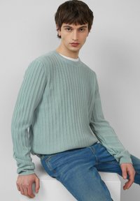 Jasnoniebieski sweter o prążkowanej strukturze, wykonany z miękkiego materiału, z okrągłym dekoltem, w połączeniu z niebieskimi dżinsami. Sweter ma długie rękawy i teksturowany wzór.