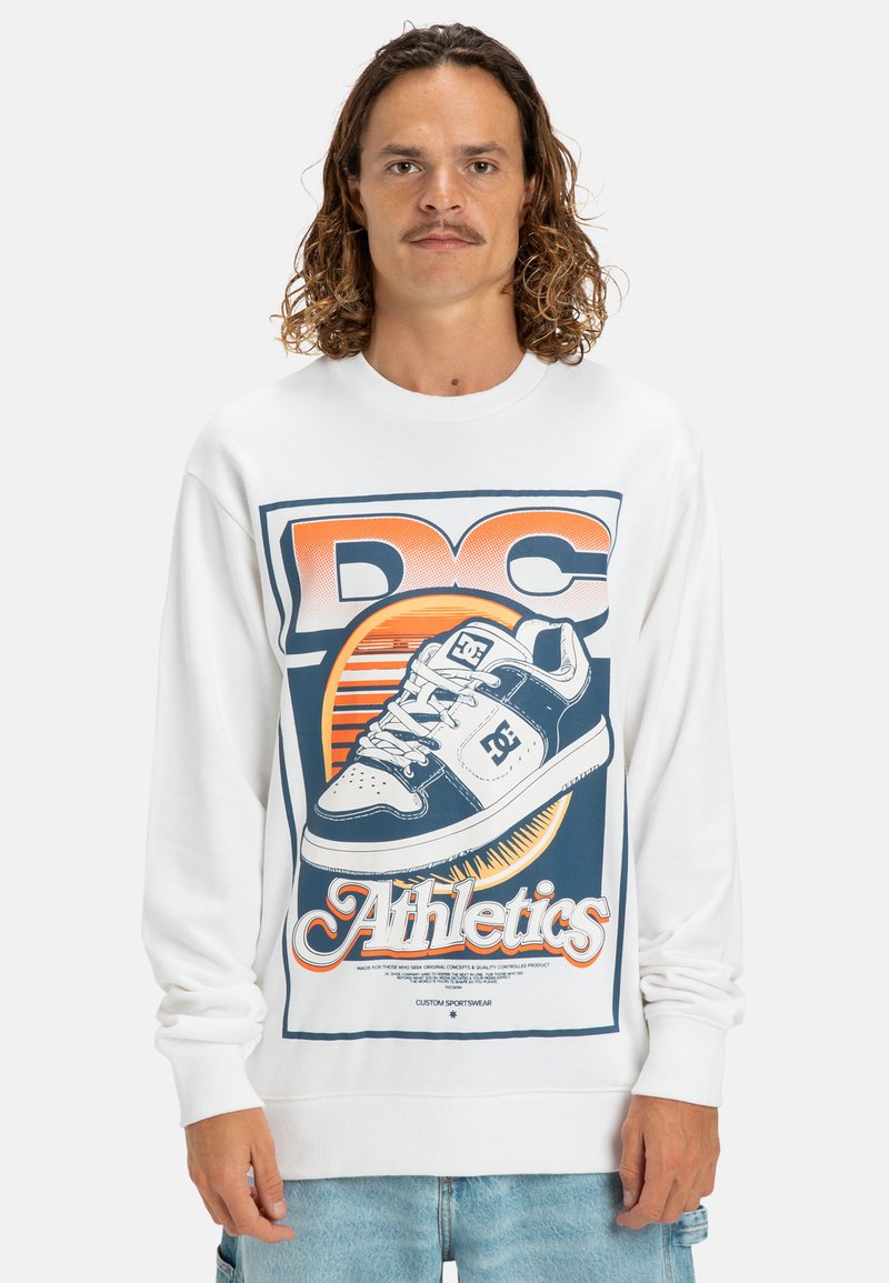 Witte sweatshirt met een grote graphic van een sneaker en de tekst "DC Athletics". Het ontwerp heeft oranje en blauwe accenten. Zachte textuur, ronde hals.