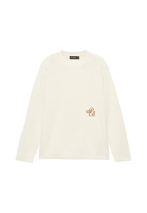 Pull tricoté couleur crème avec une texture côtelée et un petit patch brodé avec des lettres cursives "S" et "B" sur la poitrine.