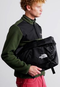 Borsa messenger nera realizzata in materiale resistente all'acqua, con logo, tracolla regolabile e un design elegante e minimalista.