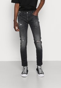 Tmavě šedé slim-fit džíny s roztrhanými detaily, pět různých kapes a zapínání na knoflík, spárované s černými vysokými teniskami a černým tričkem.