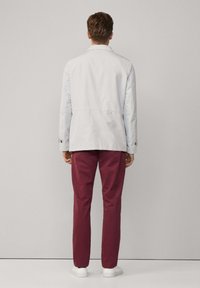 Veste gris clair à coupe droite et coutures arrière, assortie à un pantalon bordeaux. Le modèle porte des baskets blanches. Design simple, sans motifs.