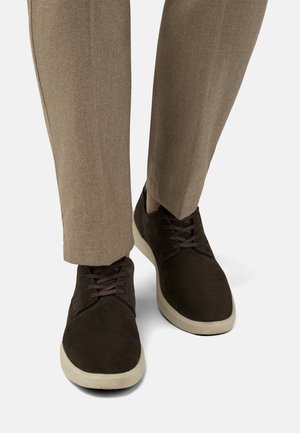 Brune ruskindsko med cremefarvede gummisåler og brune snørebånd. De er stylet med lysebrune skræddersyede bukser med en glat tekstur.