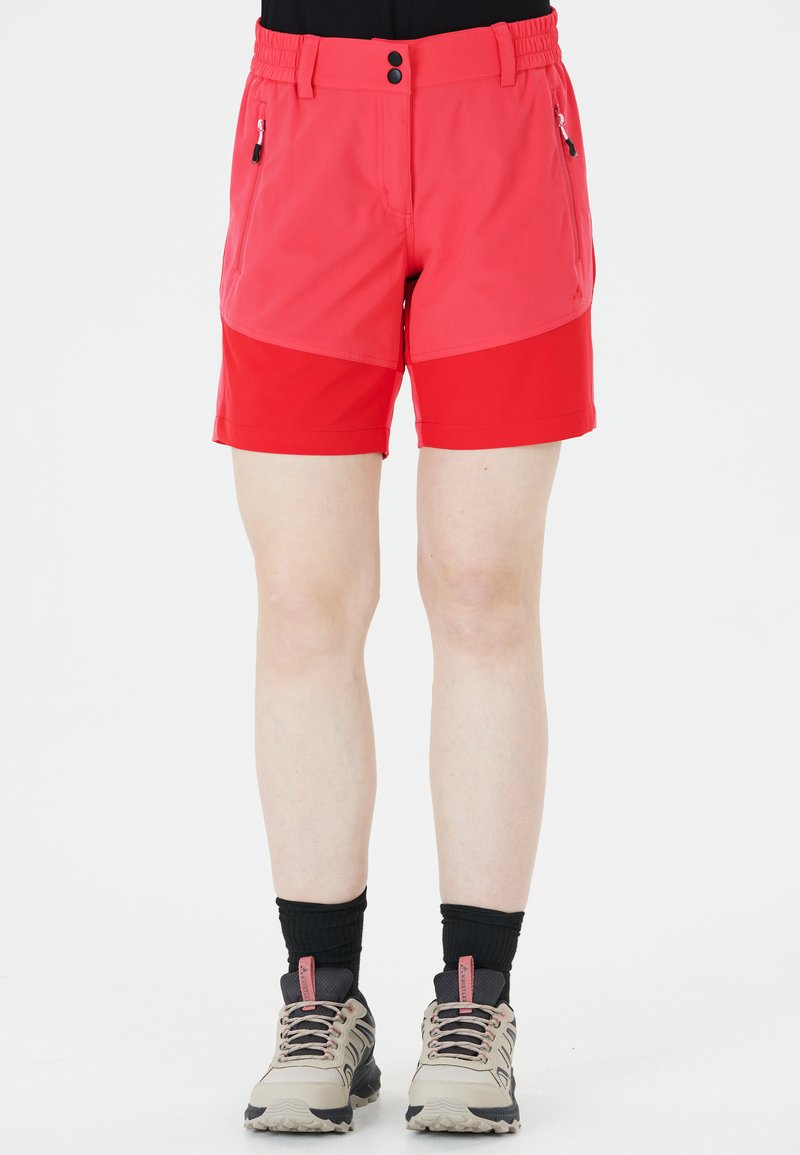 Röda shorts med elastisk midja, två sidofickor och en kontrasterande nedre panel. Tillsammans med beige vandringsskor och svarta strumpor.