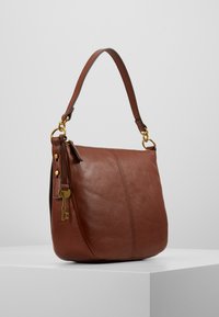 Bruine leren schoudertas met gouden accenten, een gladde textuur en een sleutelhanger eraan bevestigd. Heeft een enkele strap en een gestructureerd design.