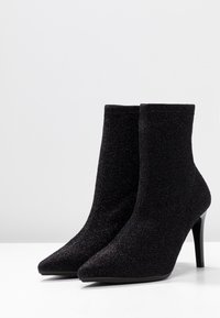 Botines negros de tobillo hechos de tela texturizada, con punta afilada y un elegante tacón de aguja. Superficie suave con un sutil brillo.