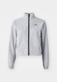 Jasnoszara kurtka wykonana z miękkiego, lekkiego materiału, z zamkiem błyskawicznym, wysokim kołnierzem oraz czarnym logo po lewej stronie klatki piersiowej.