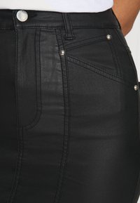 Mini-jupe en denim noir avec une texture lisse, des poches avant et des boutons métalliques en accent. Coupe ajustée avec des détails de couture décorative.