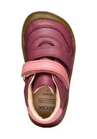 Zapato de cuero rosa y burdeos con una correa de Velcro, punta redondeada y superficie texturizada. El forro interior es de color crema y presenta el nombre de la marca.