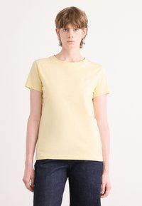 T-shirt giallo a maniche corte in cotone morbido, con scollo tondo e un logo discreto sul petto. Abbinato a jeans di denim scuro.