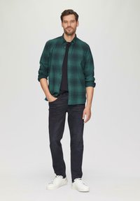 Groene geruite button-up shirt, zwarte t-shirt eronder, donkere spijkerbroek en witte sneakers. Het shirt is lichtgewicht en heeft een relaxte pasvorm.