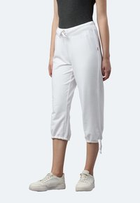 Weiße Baumwoll-Cropped-Jogginghosen mit Kordelzugbund, elastischen Bündchen, Seitentaschen und glatter Textur, kombiniert mit weißen Sneakern.