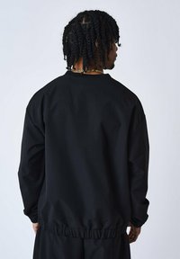 Schwarzer Rundhals-Pullover mit lässiger Passform, strukturiertem Stoff, elastischem Saum und langen Ärmeln. Ansicht von hinten.